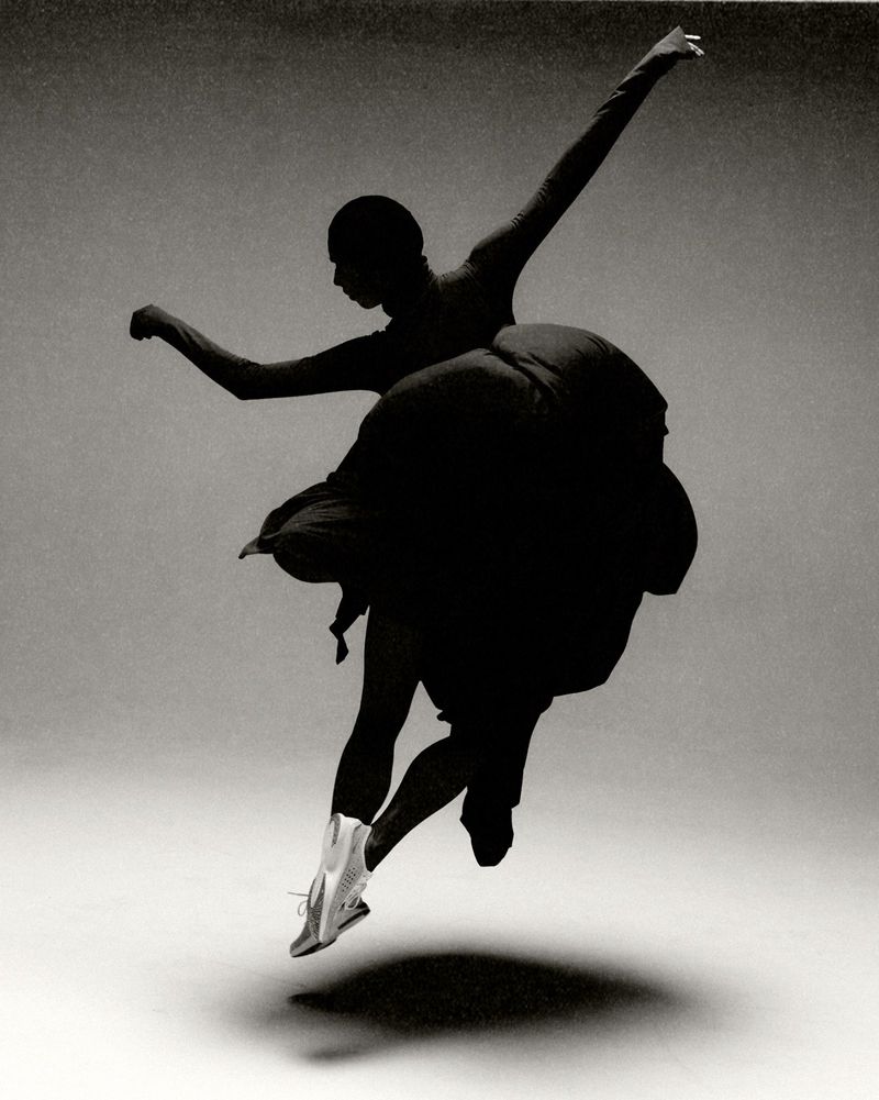 Woman in motion: Silhouette of a dancer with arms outstretched, silver dance shoes, and a flowing black dress, captured in a studio.