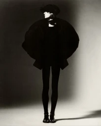 Model wearing a voluminous dark coat and hat against a grey seamless studio background for Luncheon Magazine
