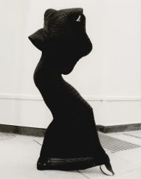 Model in a black pleated sculptural dress posing against a plain wall for Luncheon Magazine
