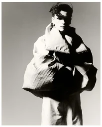 Model in an oversized sculptural jacket against a pale neutral background in high-contrast monochrome.