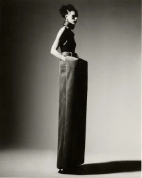 Model standing in profile wearing an oversized belted trouser and dark top against a neutral studio background.