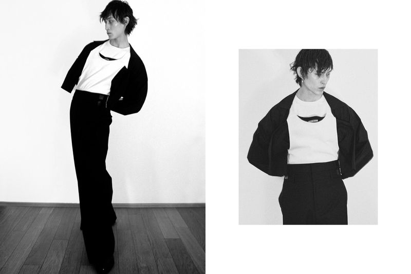 Full-length black and white shot of a slender adult in black wide-leg pants and jacket over a white top, striking a fashionable pose.