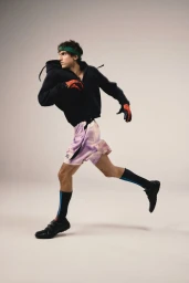 Male model in a black hoodie and patterned shorts running against a neutral grey studio backdrop