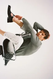 Model Eliott Tipp seated in a modern chair wearing a green sweater against a white backdrop