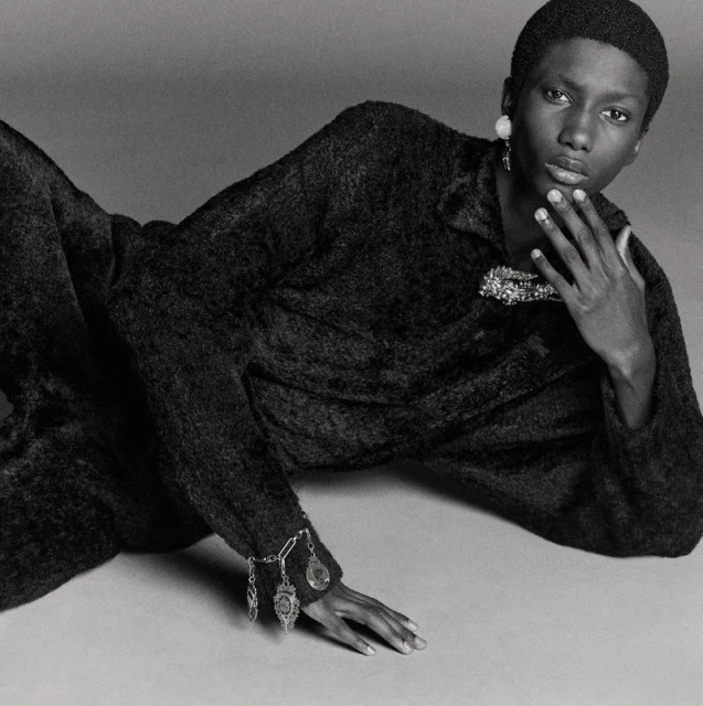 Fashion portrait of a black woman with short hair wearing a dark, textured two-piece outfit with jewellery in a studio setting.