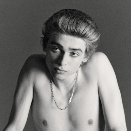 Black and white portrait of a young adult male with fair skin and light brown hair, wearing a silver chain necklace.