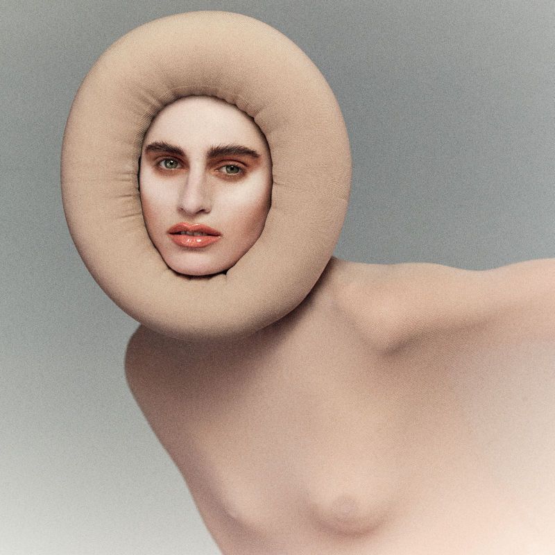 Fashionable woman with nude body paint and a beige, ring-shaped headpiece in a studio shot showcasing beauty and artistry.