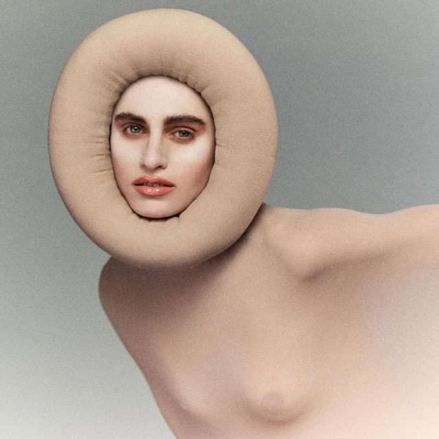 Fashionable woman with nude body paint and a beige, ring-shaped headpiece in a studio shot showcasing beauty and artistry.