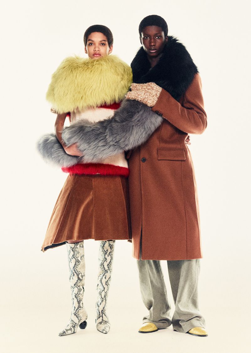 Two fashion models pose in a studio wearing coats and statement accessories, including faux fur and snake print boots.