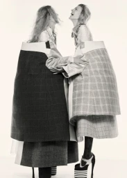 Two female models wearing structured plaid coats laughing together against a bright white background for System Magazine.