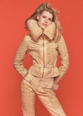 Model wearing a textured cream leather jacket and matching pants against a solid orange background