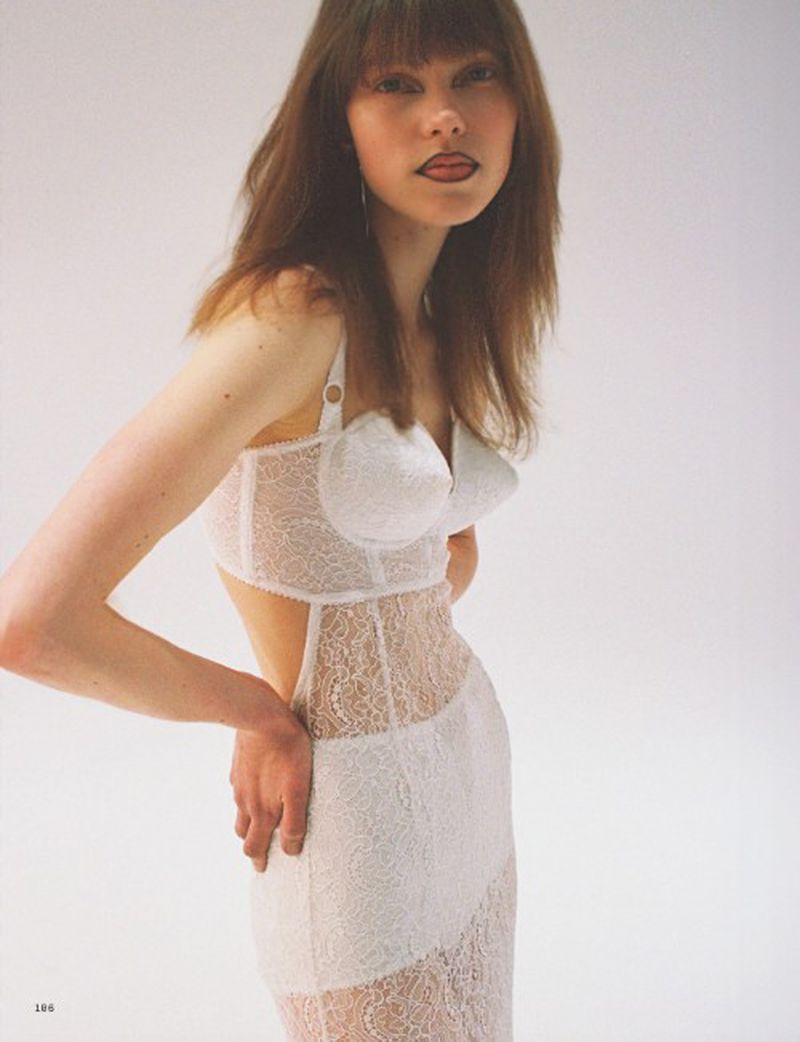 A slender woman poses in a white lace gown against a bright white backdrop, showcasing a modern and stylish fashion aesthetic.