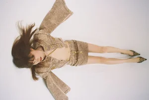 Model lying on white floor wearing textured tan denim jacket and matching skirt with pointed shoes