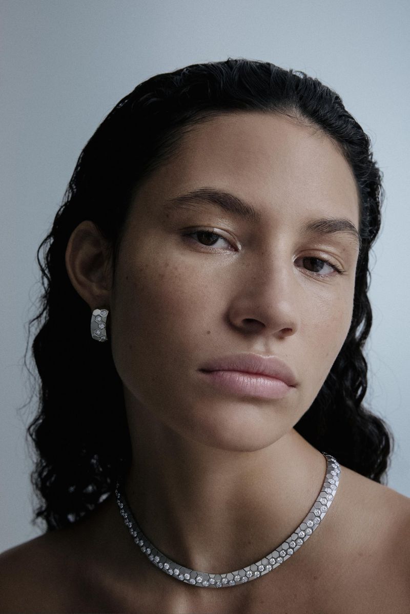 Close-up of an adult female model with black hair, wearing jewelry, including a necklace and earrings, against a neutral background.
