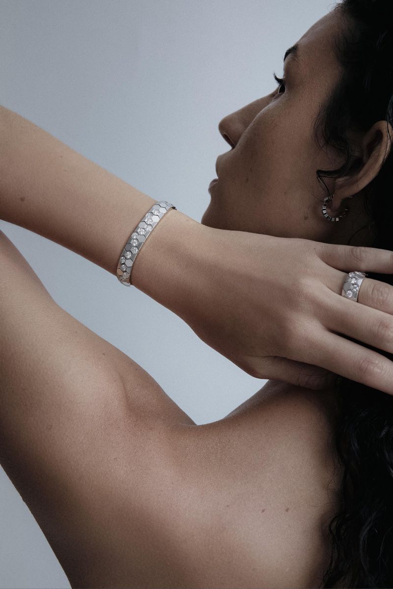 Close-up of an adult woman's arm and hand showcasing a silver bracelet and ring with stone details against a light gray background.