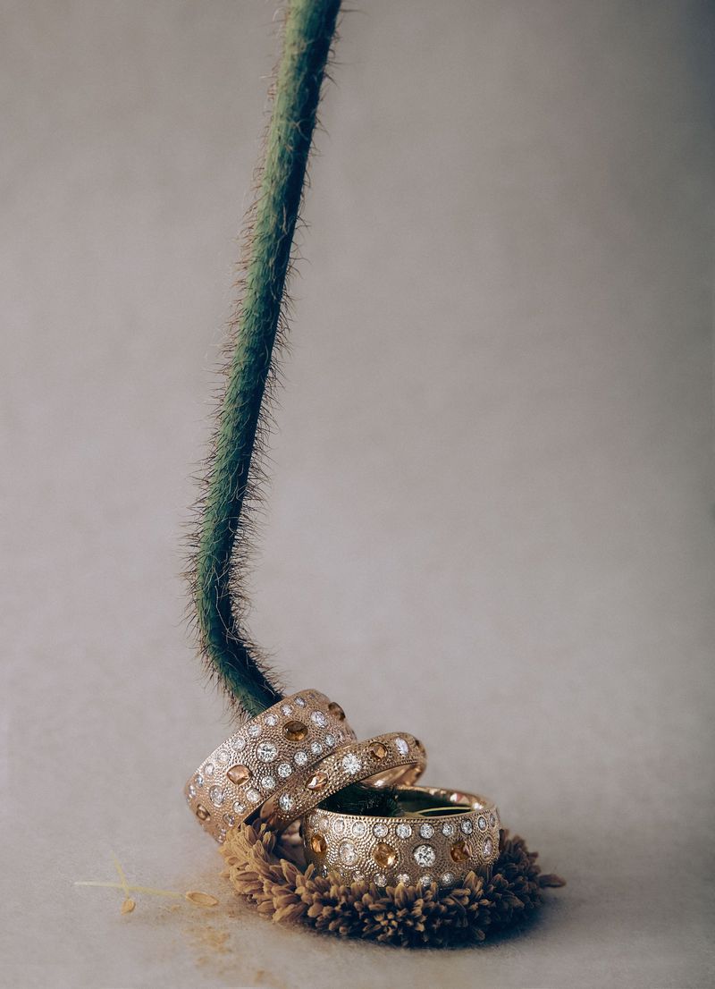 Elegant jewelry composition: Three gold bangles adorned with clear and amber gems, arranged on a soft, textured surface with a green stem.