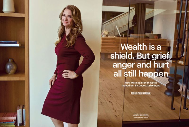 Melinda French Gates poses in a burgundy dress next to a bookshelf in an office setting with a glass door displaying a quote.