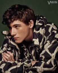 Sam Nivola wearing a patterned hooded jacket against a dark green backdrop for V Man