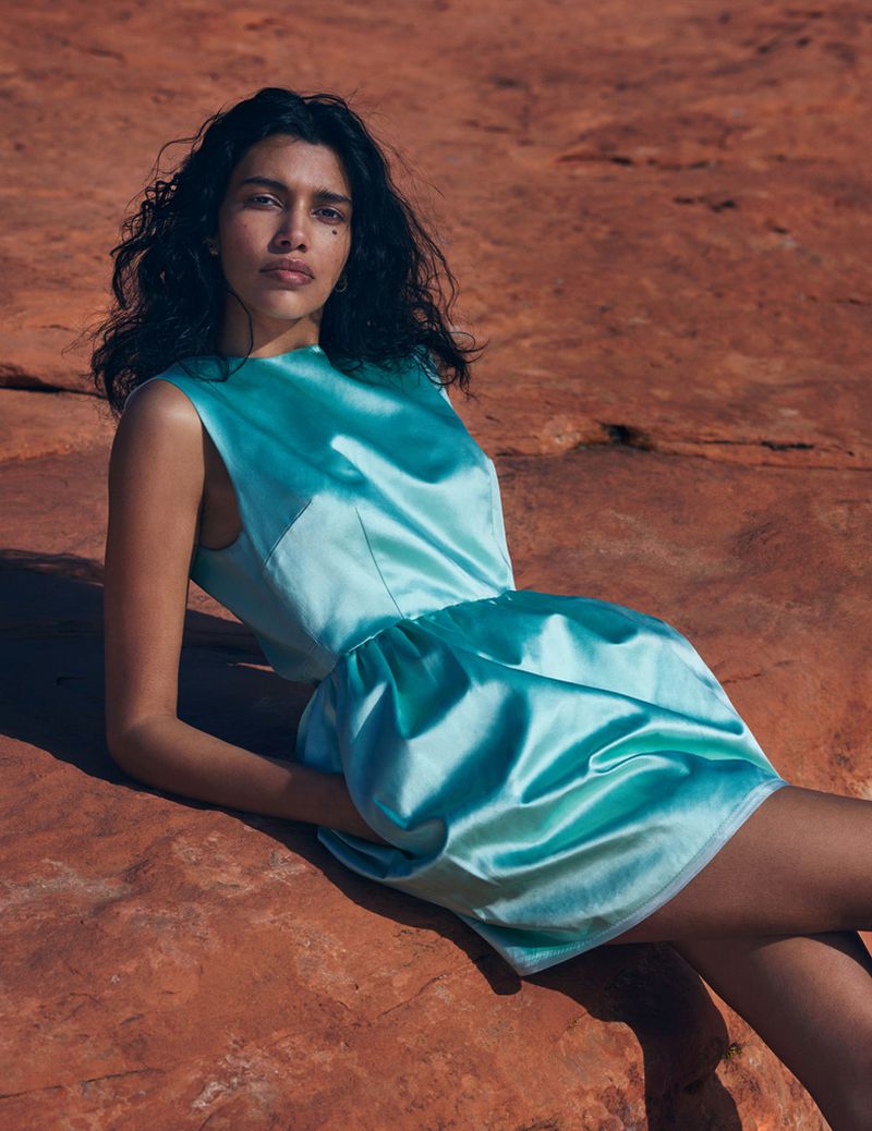 Woman in aqua mini dress poses on red rock formations, creating a striking fashion editorial with natural desert backdrop.