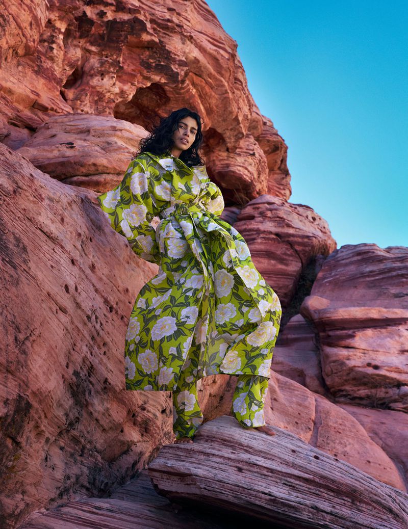 A woman in a floral outfit poses on rocks in a desert landscape under a blue sky, showcasing an outdoor fashion editorial shoot.