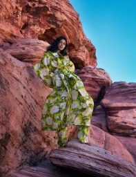 Model Pooja Mor posing in a green floral coat among red rock formations for The Hunger Magazine