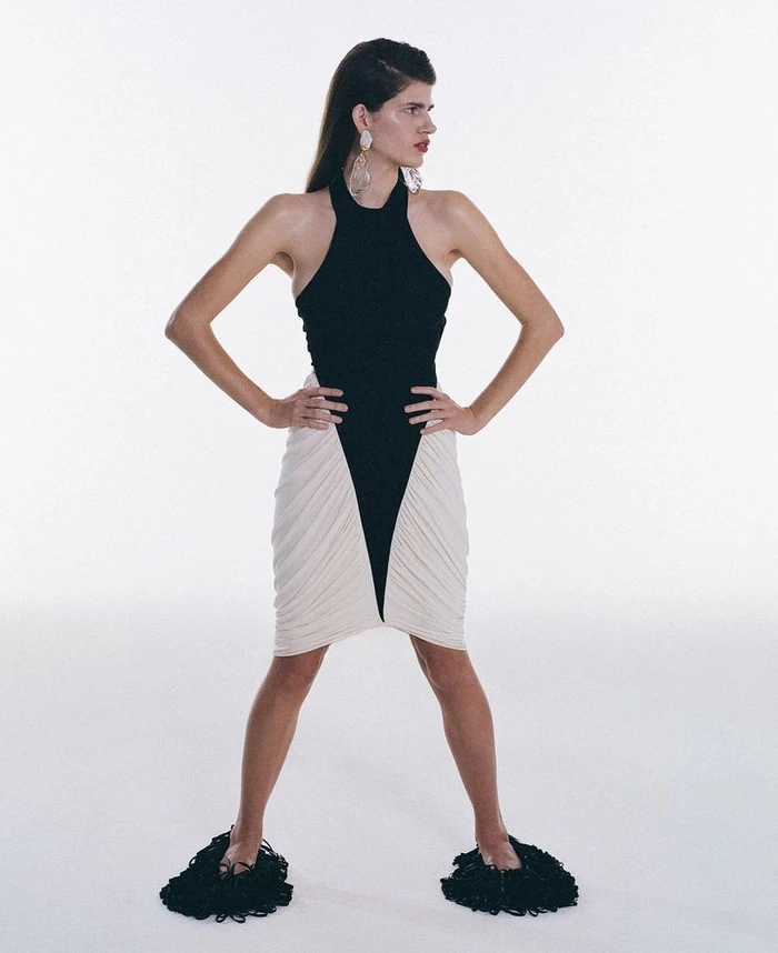 Model wearing a black halter dress with white paneling and dark textured footwear standing against a plain background