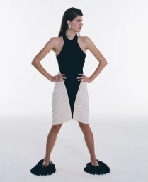 Model wearing a black halter dress with white paneling and dark textured footwear standing against a plain background