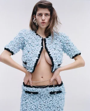 Model wearing a textured light blue cropped jacket and matching skirt against a plain white background