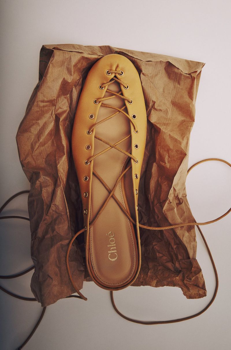 Overhead shot of a Chloe ballerina flat shoe with laces on crinkled brown paper, emphasizing its design and stylish presentation.