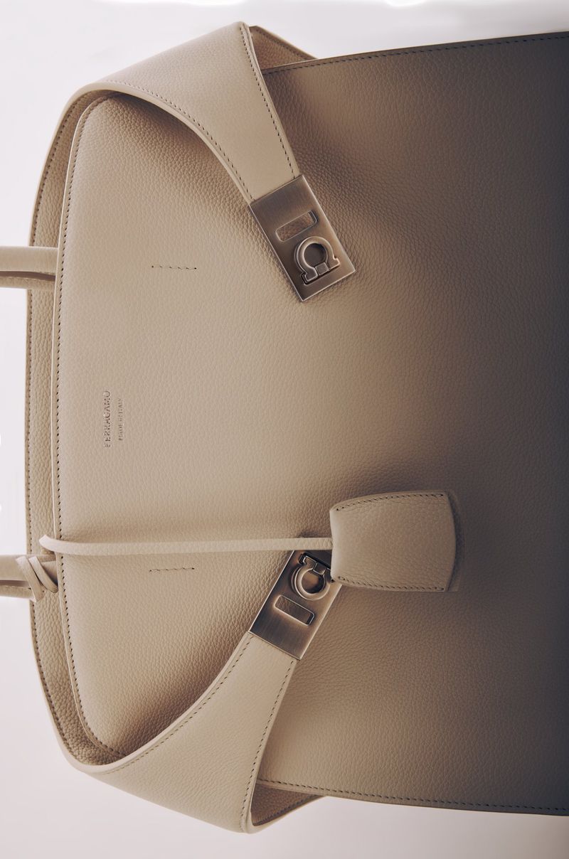 Elegant beige leather tote bag with silver hardware, featuring a shoulder strap and structured design, set against a light background.
