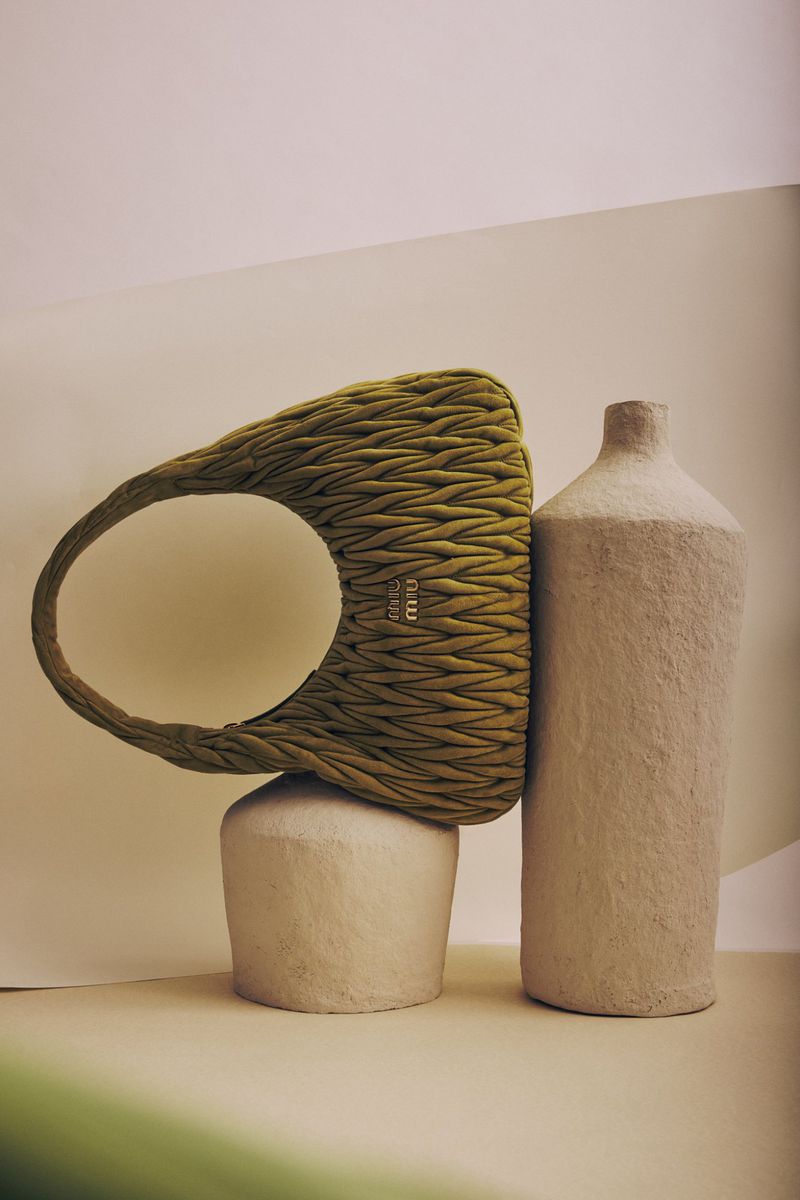 Miu Miu woven bag in green and beige, displayed with beige sculptural forms in a studio setting, showcasing high-fashion accessory.