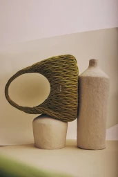Olive green quilted shoulder bag resting on textured sculptural ceramic vessels against a neutral background.