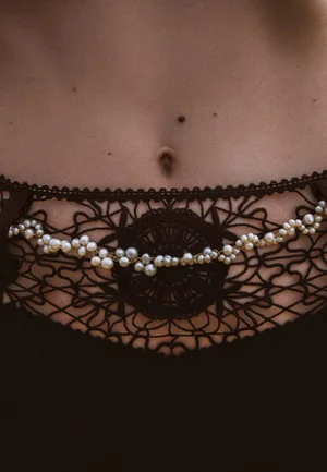 Close-up of a model wearing dark lace lingerie adorned with a delicate pearl body chain across the waist for JANE by the Grey.