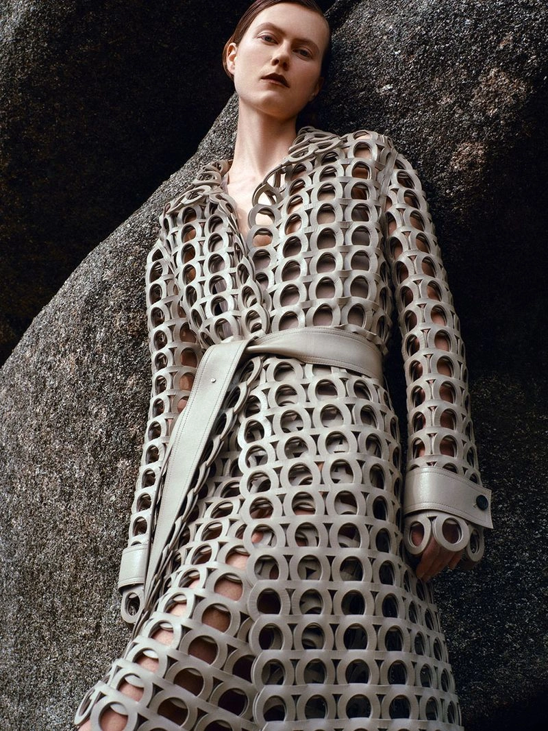 Model in a cut-out patterned grey coat posing against large natural rock formations for Harper's Bazaar UK editorial.
