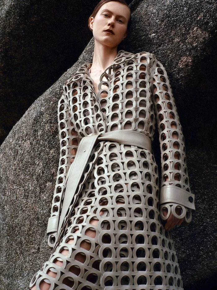 Model in a cut-out patterned grey coat posing against large natural rock formations for Harper's Bazaar UK editorial.