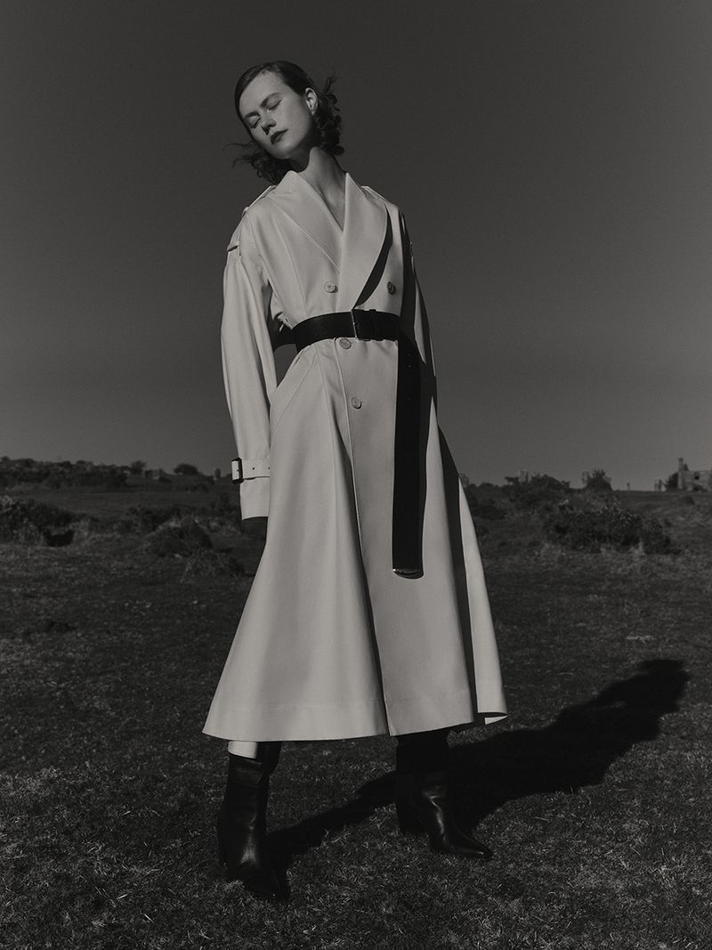 Model wearing a belted white coat outdoors against a dark sky and low horizon landscape for Harper's Bazaar UK editorial.