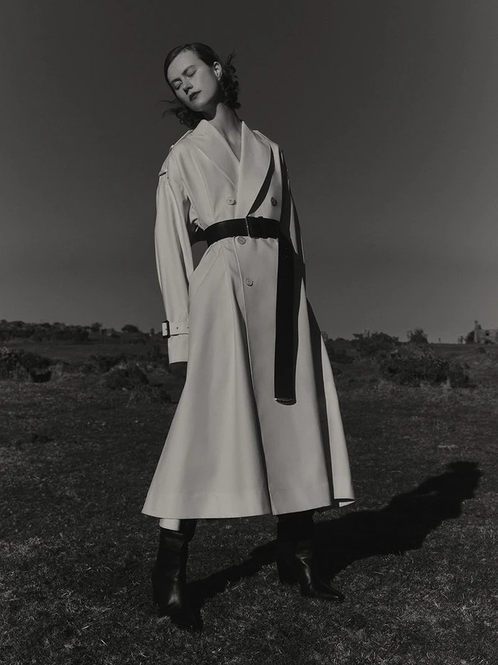 Model wearing a belted white coat outdoors against a dark sky and low horizon landscape for Harper's Bazaar UK editorial.