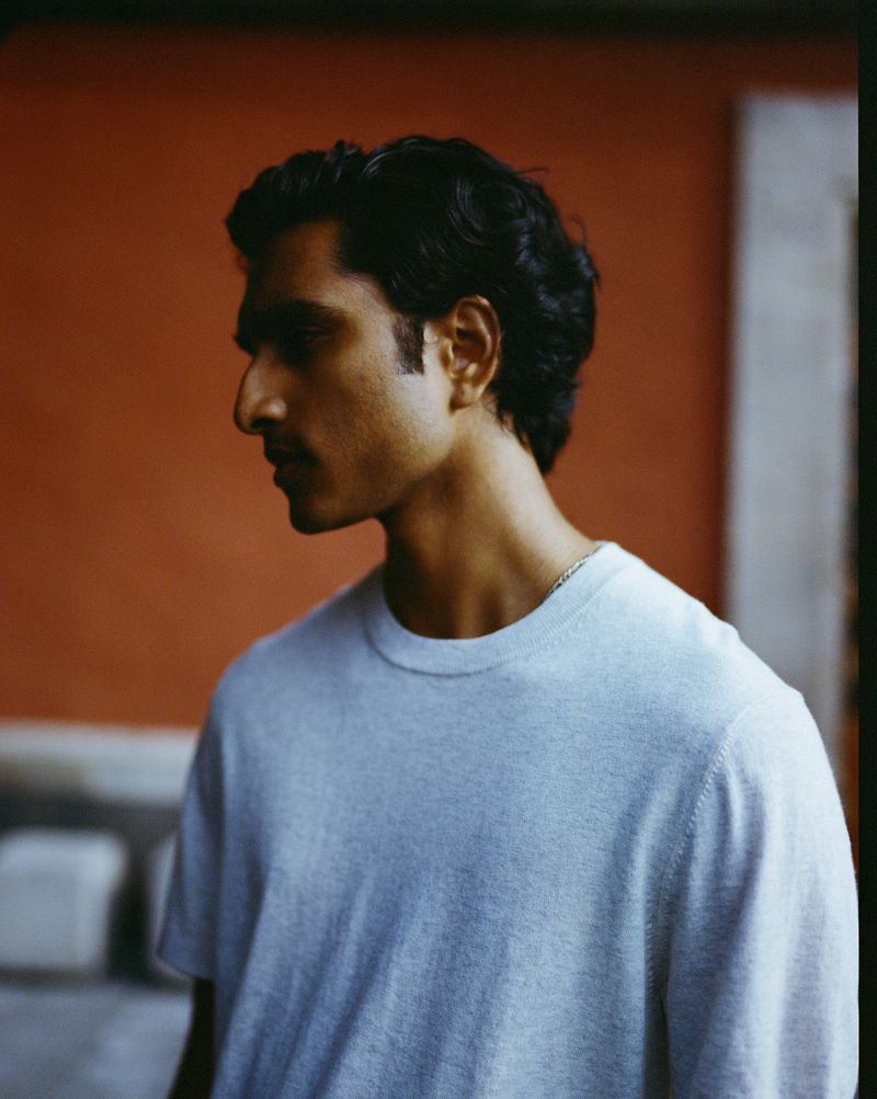 Portrait of a man in a light blue t-shirt standing indoors with a red wall in the background, captured in a medium shot.