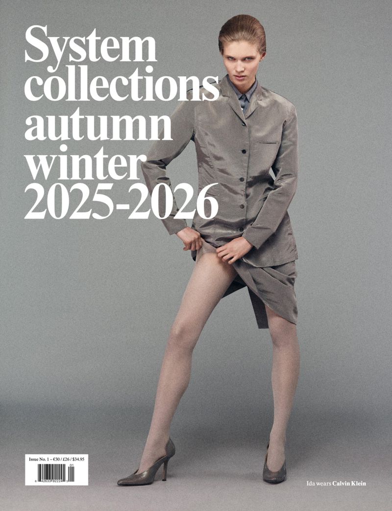 Fashion magazine cover featuring a woman in a grey suit and pantyhose, striking a pose against a grey backdrop with bold text.