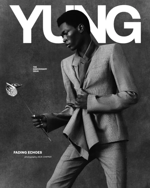 Magazine cover features a Black male model in a gray plaid suit holding a silver calla lily against a gray backdrop with large white text.