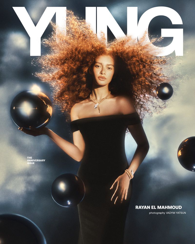 Model Rayan El Mahmoud wearing an off-shoulder black dress with floating dark spheres in a magazine cover editorial