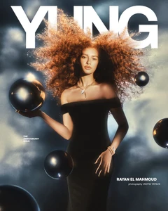 Model Rayan El Mahmoud wearing an off-shoulder black dress with floating dark spheres in a magazine cover editorial