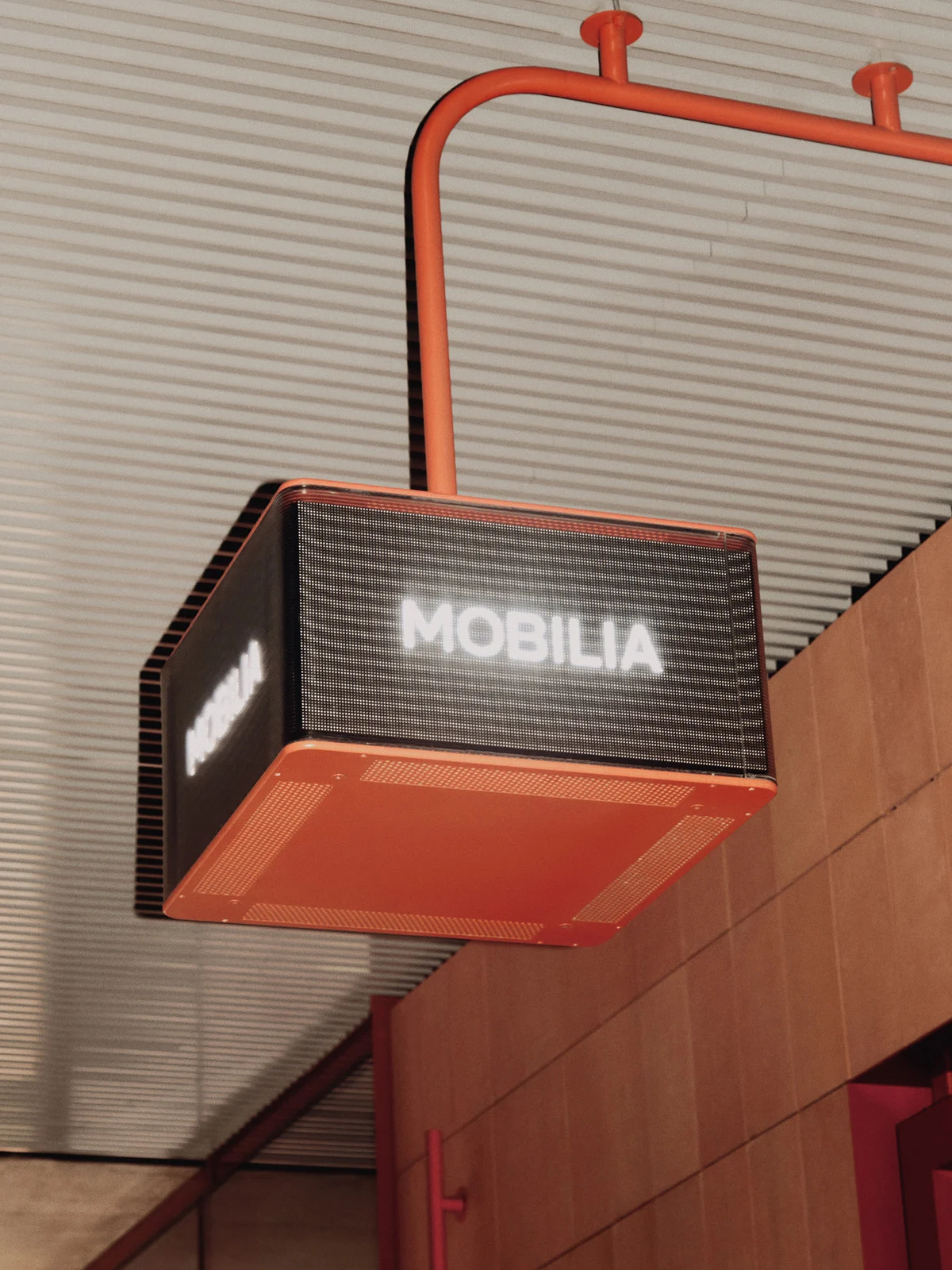 Illuminated sign displays the word MOBILIA in bright white letters, mounted under a ceiling with orange support beams, indoor shot.