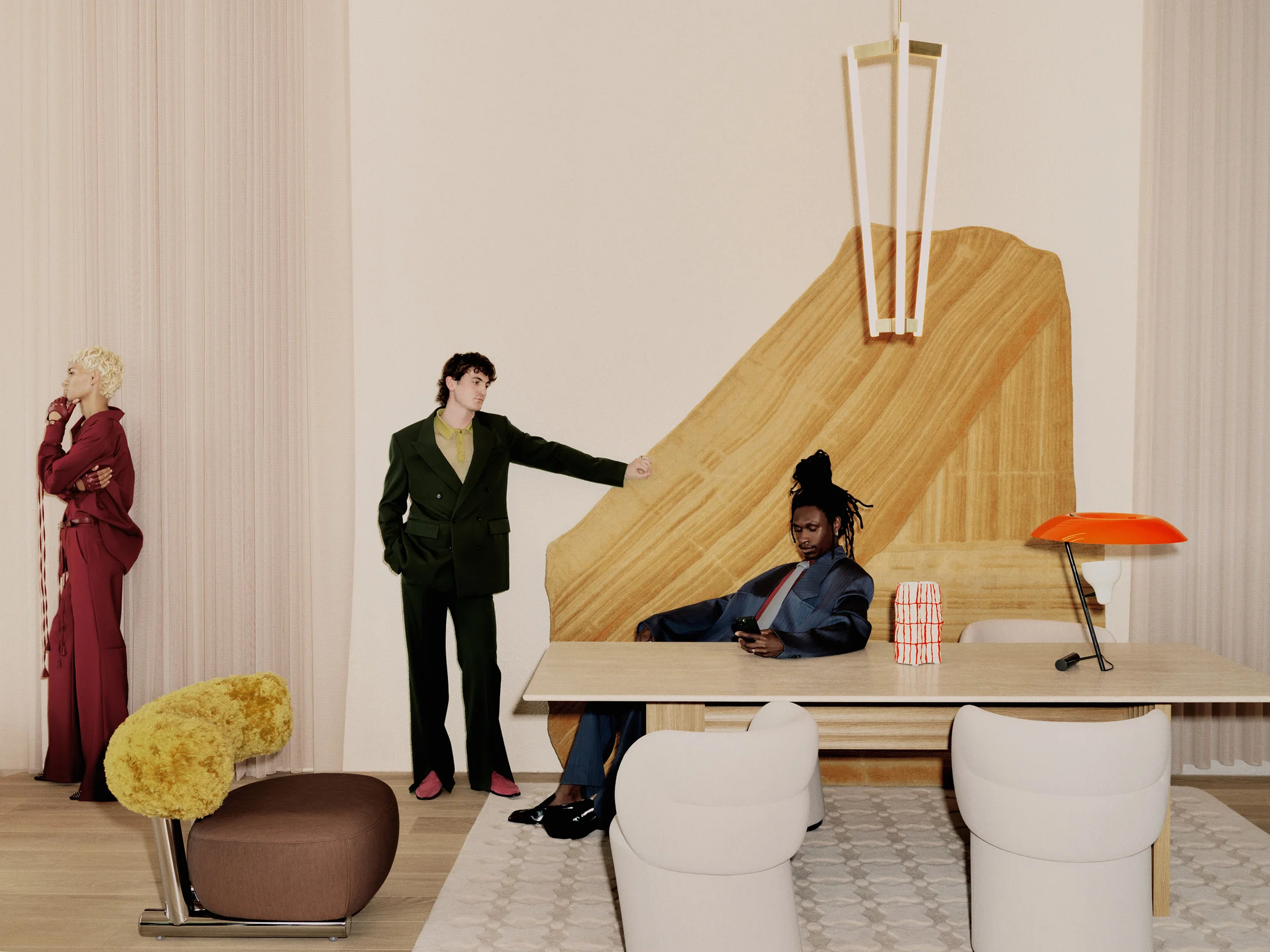 Three people are posing in an indoor setting next to modern furniture including chairs and tables, illuminated by a modern lighting fixture.