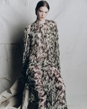 Model seated against a textured backdrop wearing a long-sleeved floral print dress by Lee Mathews for AFW Resort 26.