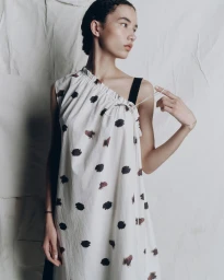 Model wearing a white patterned dress against a textured backdrop for the Lee Mathews AFW Resort 26 campaign.