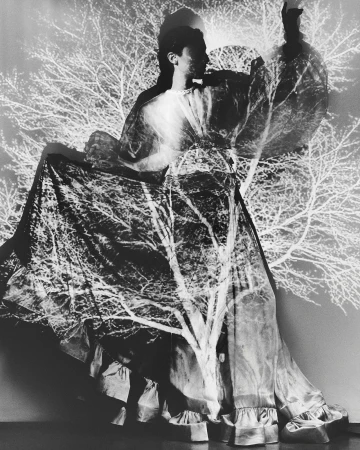 Monochrome double exposure of a woman in flowing dress, superimposed with bare tree branches creating a ghostly, surreal composition.