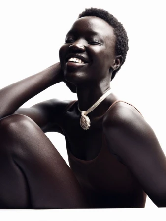 Close-up of smiling African woman wearing a brown top and white statement necklace against a white backdrop in a studio shot.