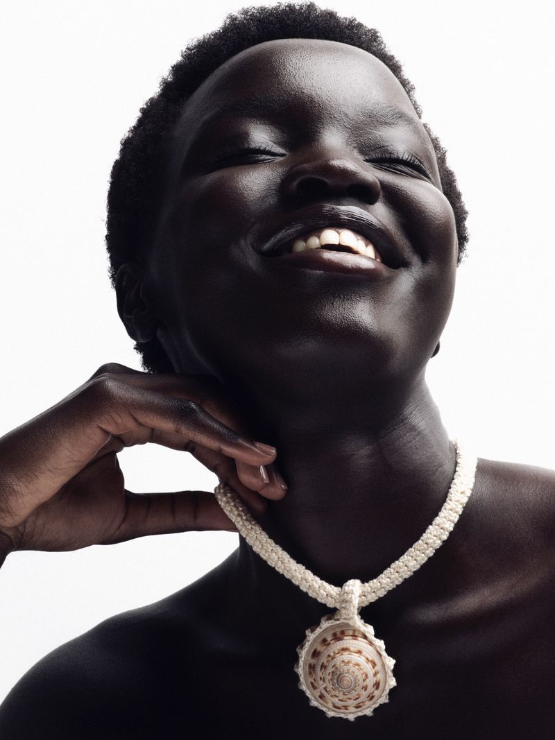 Close-up studio shot of a smiling Black woman wearing a shell necklace against a white background with soft, diffused lighting.