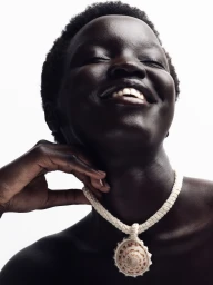 Close-up portrait of a smiling Black woman wearing a shell pendant necklace against a plain white background.